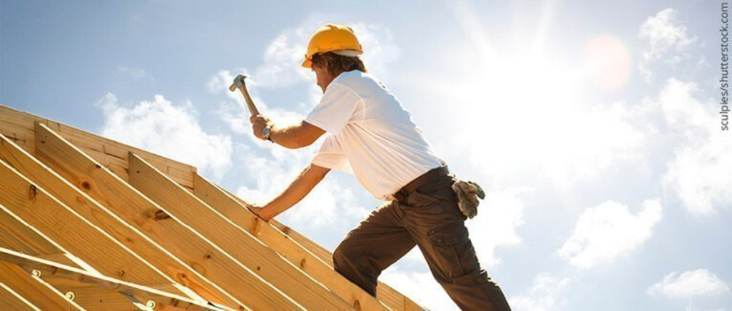 Situativ: Handwerker mit Helm arbeitet mit Hammer auf Dachstuhl